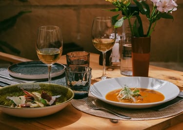 Mesa montada con comida encima, se ve deliciosa, alcachofas y sopa de pescado. Hay flores bonitas en el restaurante Es Mestra