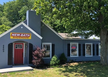 Front view of the New Bath Elite showroom in Perrysburg, Ohio, featuring a gray building with a red door, bright yellow logo