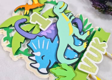 Colorful paper cake topper featuring a cartoon dinosaurs theme with the number "1" at the center. Th