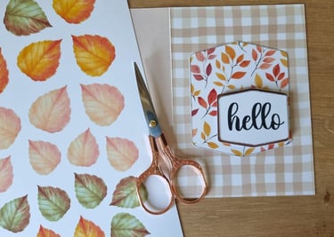 A crafting setup on a wooden table with scissors and fall card