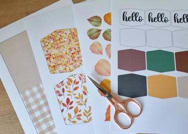 Crafting materials on a wooden table include colorful papers with autumn leaves and fall colors