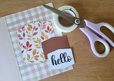Greeting card materials on a wooden table, featuring autumn leaf patterns