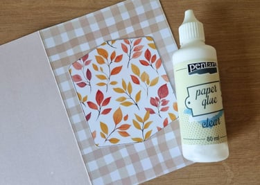 An open greeting card with checkered beige and white patterns, featuring a cutout with autumn leaves