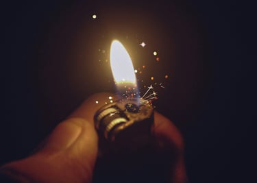 A hand holding a lit cigarette lighter at night