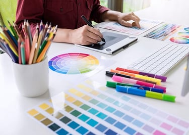alt="Graphic design computer work station with assorted color samples pencils and pens"