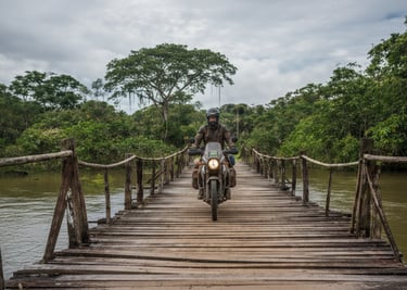 A motorcyclist crossing a wooden bridge over a river in a lush green forest.