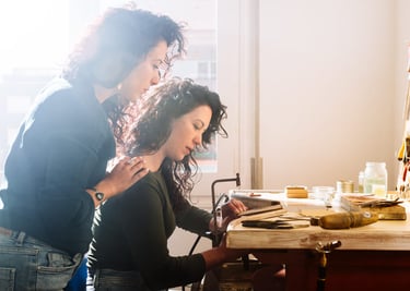 Dos artesanas creando piezas a mano en un taller luminoso.”