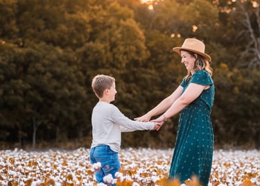 Mom laughing and holding her son's hands in a cotton field during the evening golden hour. 