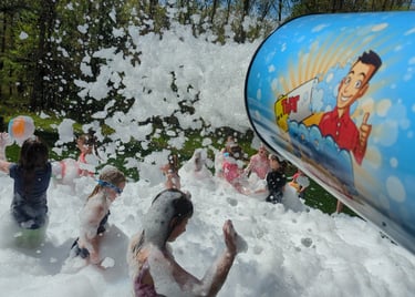a group of children playing in foam with a foam machine blasting at a birthday party
