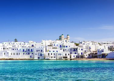 Scenic view of white houses and blue windows in Naoussa, Paros island, overlooking turquoise Aegean Sea water.