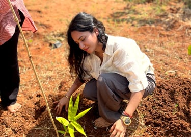 A young girl planting a bamboo sapling in fertile red soil during a community gardening event.