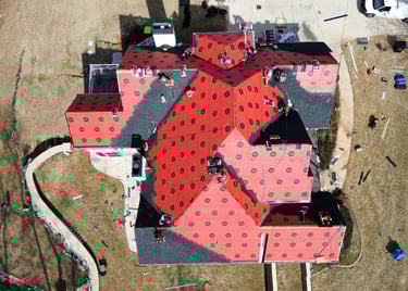 Aerial drone view of professional roofers installing new asphalt shingles over red underlayment on a residential home.