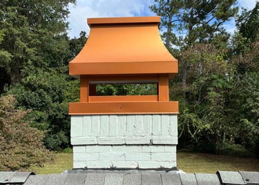 Custom copper-colored metal chimney shroud installed on a white brick chimney cap atop a shingle roof.