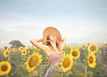 A joyful woman in straw hat standing in a sunflower field with arms outstretched, embracing the sun