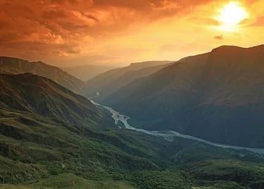 Golden sunset over a deep mountain valley with a winding river flowing through the canyon.