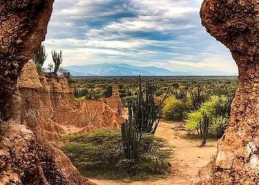 A scenic view of the Tatacoa Desert in Colombia framed by a natural rock window with cacti and red sand.
