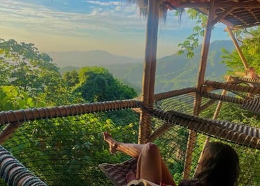 A woman relaxes in a net hammock at a tropical mountain eco-resort while reading a book.