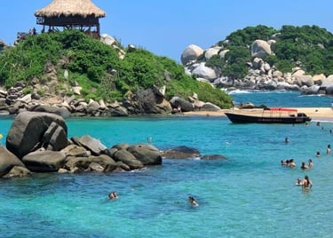 Tropical beach at Tayrona National Park in Colombia with clear turquoise water and a thatched hut on a rocky hill.