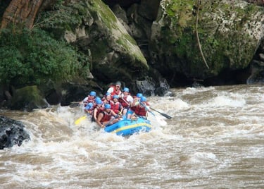 A group of people wearing helmets and life jackets white water rafting down a river with rocky banks.