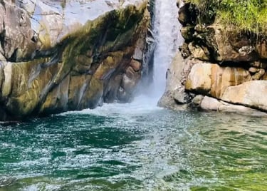 A scenic tropical waterfall flowing into a clear turquoise natural pool surrounded by rocks and lush green trees.