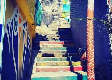 Vibrant street art mural of a child’s face overlooking colorful painted stairs in a narrow alleyway.