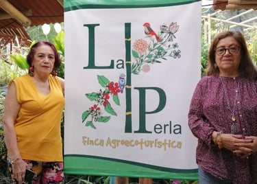 Two women, possibly owners, stand proudly beside a banner for "La Perla Finca Agroecoturística," a sustainable eco-tourism