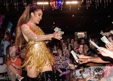 girly drag queen dressed in gold, dancing and accepting tips from eager, happy audience.