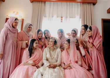 Smiling bride in white lehenga surrounded by bridesmaids in pink hijabs at a traditional Nikah ceremony.