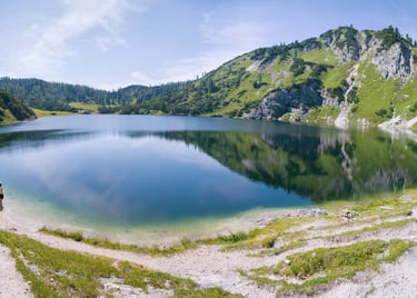 Panoramic view of a crystal clear alpine lake surrounded by green mountains and hiking trails.