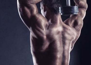 Muscular man performing overhead tricep extensions with a heavy dumbbell to build back and arm muscles.