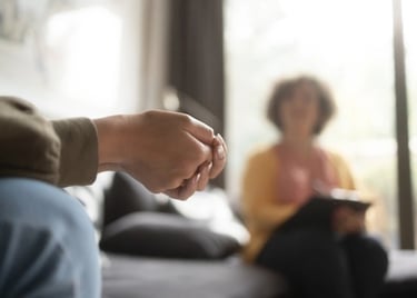 Gros plan des mains d'une personne en séance de thérapie, avec une personne qui prend des notes en arrière-plan.