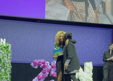 Dos mujeres afro abrazandose una de ellas sujetando un premio