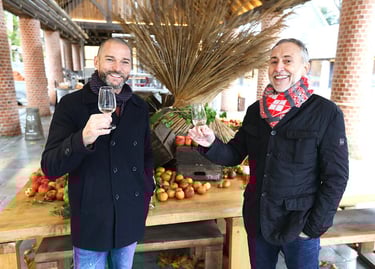 two men standing next to each other holding wine glasses