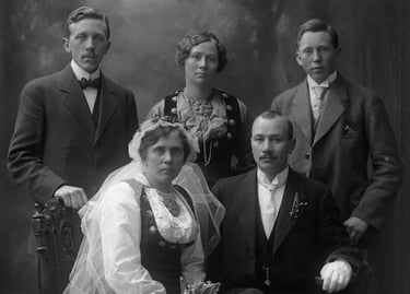 Two mend and a woman stand behind a bride and groom, black and white, the women in bunad