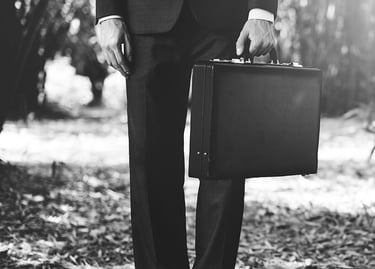 Foto a blanco y negro mostrando de la cintura para abajo un hombre con traje y maletín en mano.