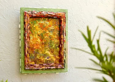 Abstraktes Bild mit Rahmen aus kleinen dunklen Holzscheiten und einem weiteren, grünen Betonrahmen