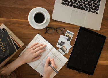 Une personne écrit sur un cahier sur une table avec un ordinateur portable à côté