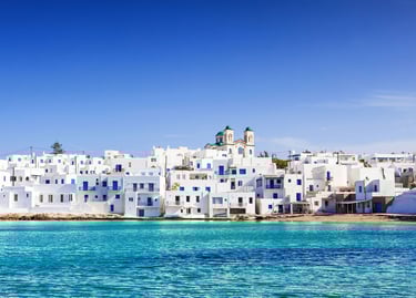 Scenic view of white houses and blue windows in Naoussa, Paros island, overlooking turquoise Aegean Sea water.