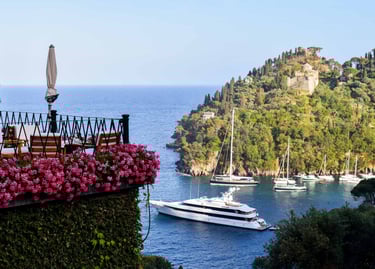 Luxury terrace with pink flowers overlooking yachts in the blue waters of Portofino, Italy.
