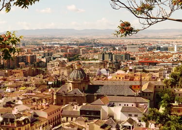 Panoramic cityscape view of Granada, Spain, featuring red-tiled roofs and the historic church of San Jeronimo.