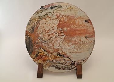 Round fluid acrylic pour painting with orange, white, and black cells on a wooden display stand.