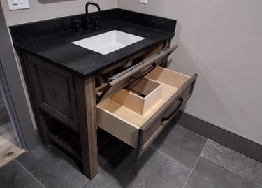 Rustic wood bathroom vanity with black granite countertop, matte black faucet, and open storage drawer.