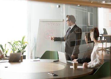Professional businessman leading a corporate team meeting and pointing to a whiteboard diagram.