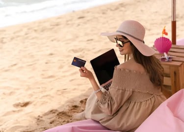 Woman using a credit card and laptop for online shopping while relaxing on a sandy beach.