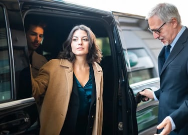 Professional chauffeur opening a black luxury car door for business travelers at an airport.