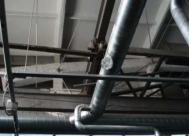 Industrial HVAC spiral ductwork and ventilation pipes installed on a warehouse ceiling.