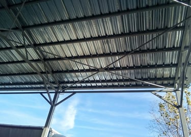 Underside of a modern metal carport roof with steel frame trusses against a blue sky.