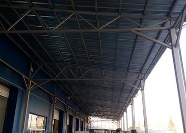 Industrial warehouse loading dock with a corrugated metal canopy and steel truss roof support structure.