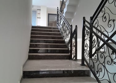 Modern interior staircase featuring dark marble steps and decorative wrought iron railings.