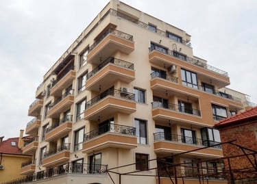 Modern multi-story apartment building with balconies and wrought iron railings under a cloudy sky.